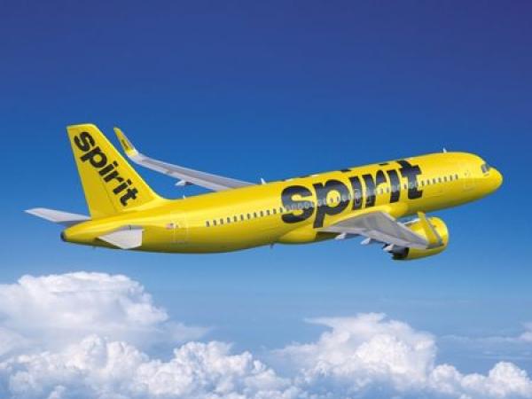 A Spirit Airlines airplane soars through blue skies.